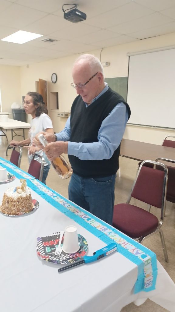 Man at a table adjusting a device, with cake and a decorated table in a classroom or meeting room