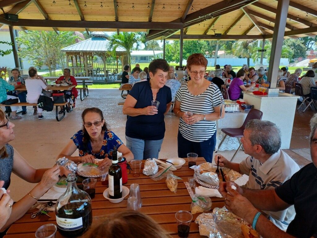 People dining at a wooden picnic table in an open-air pavilion, with drinks and food on the table.