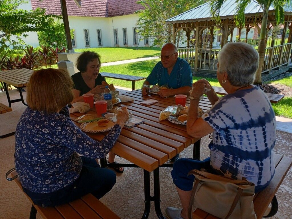 People seated around a wooden picnic table eating outdoors in a garden courtyard