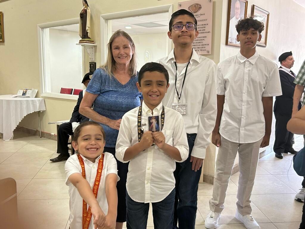 Group of five people posing indoors at a formal event, wearing white shirts and smiling.