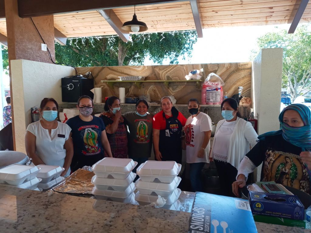 Volunteers wearing masks stand behind stacks of boxed meals at a community distribution table.