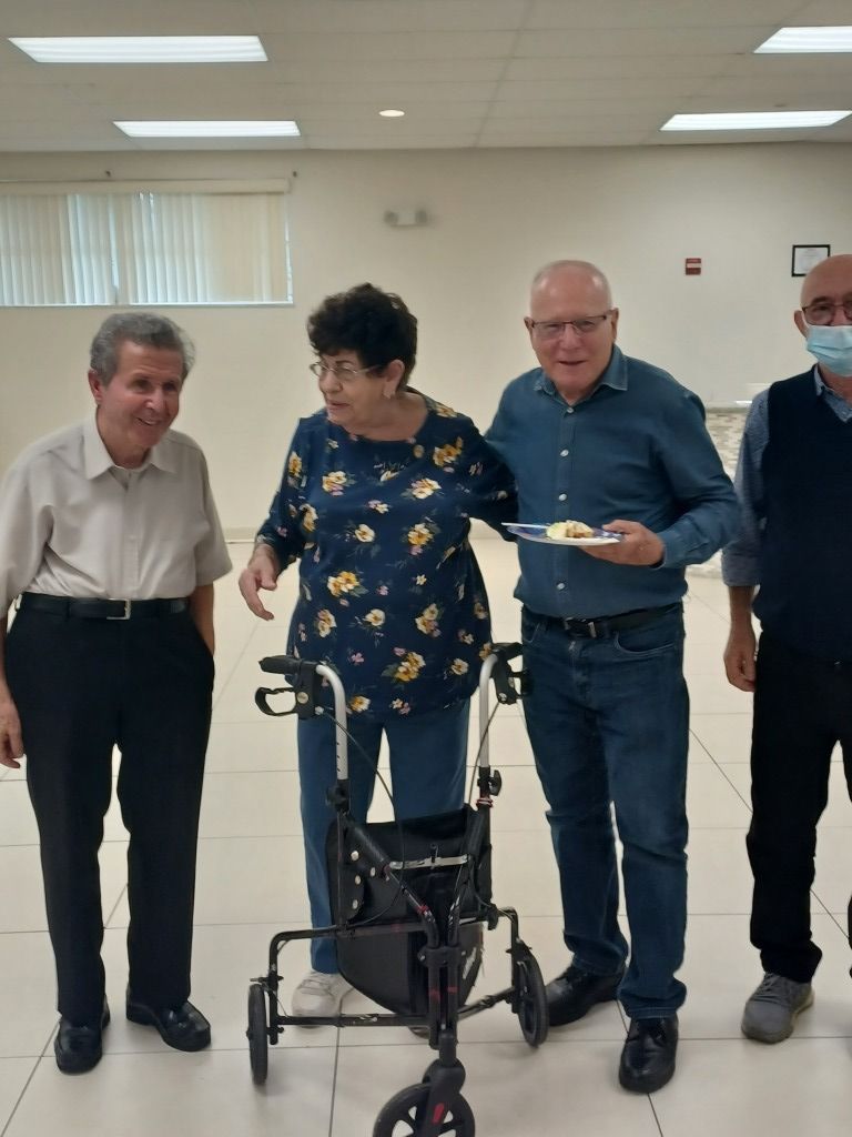 Four people standing indoors beside a rollator walker, one holding a plate, in a bright hallway
