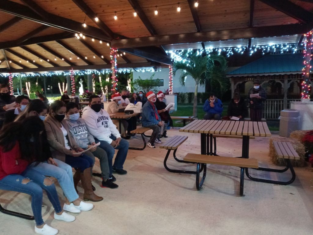 People seated in a covered pavilion with picnic tables and string lights at an outdoor gathering