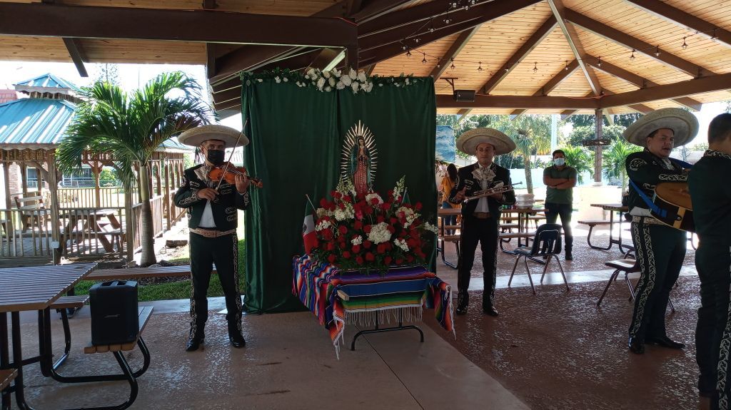 People standing under a pavilion beside a decorated altar with flowers and red-white-blue ribbons