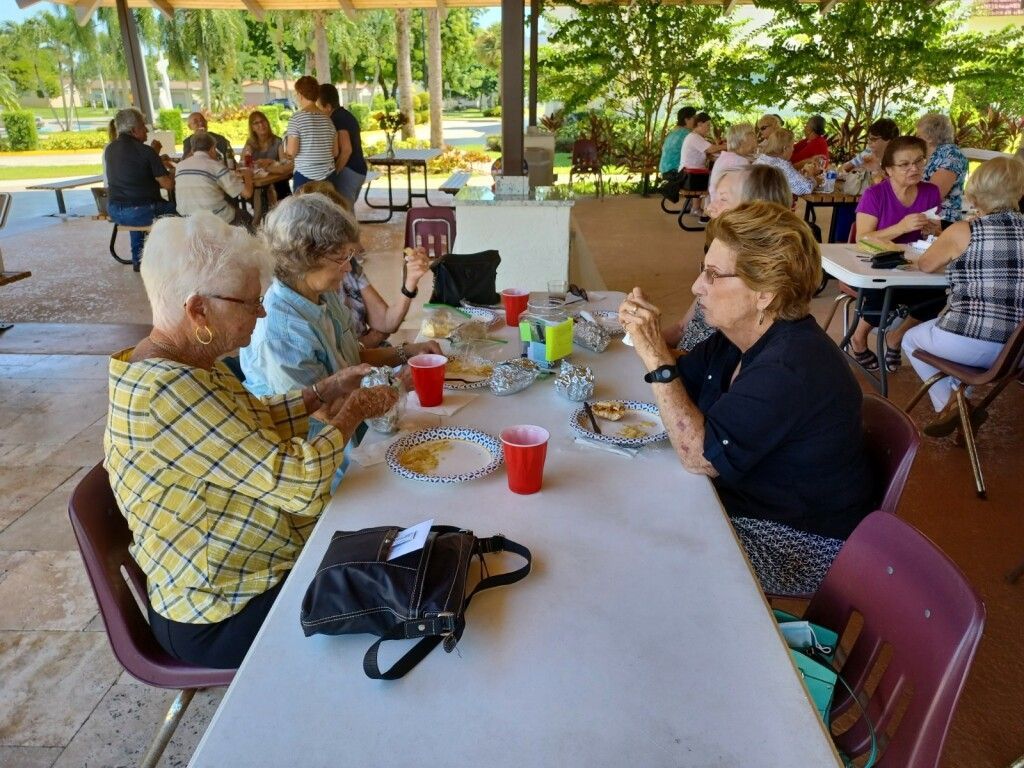People eating and talking at a picnic table under a pavilion in a park