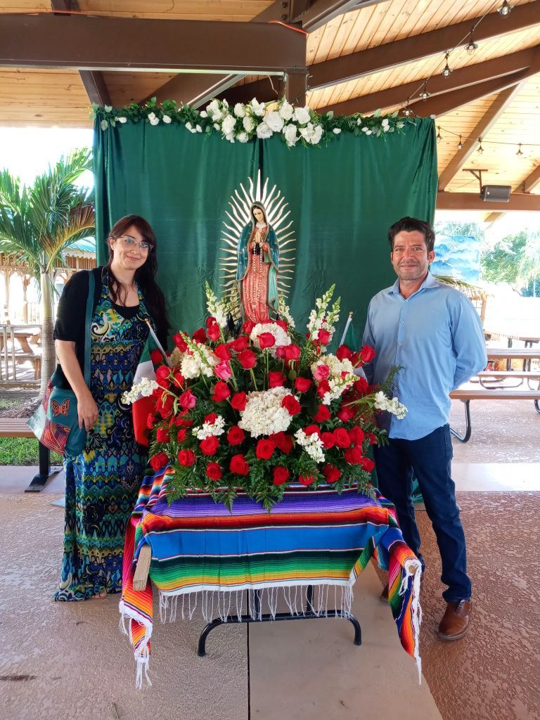 Two people standing beside a large flower altar with a religious statue in a pavilion