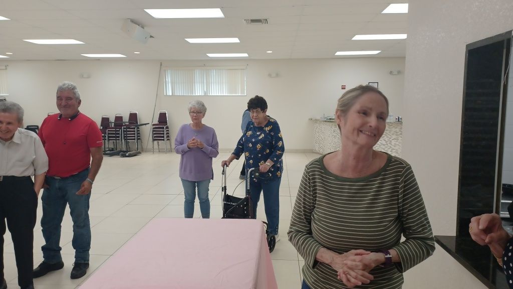 People standing in a bright community hall, with tables and chairs in the background.