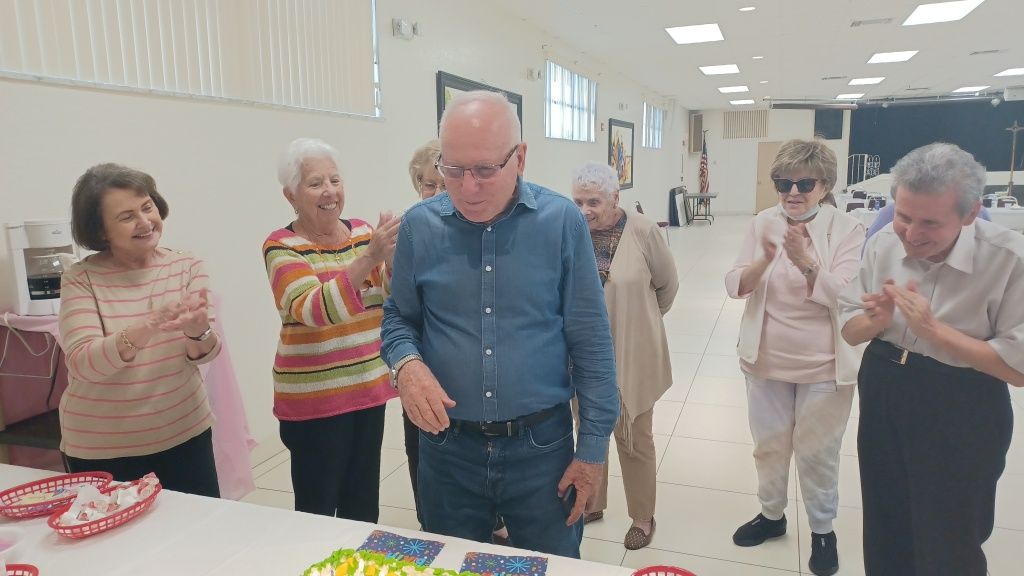 People gathered around a table, applauding during a celebration in a bright room.