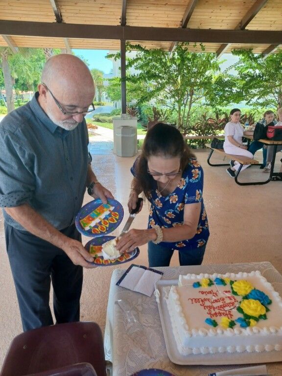 Two people cutting a decorated sheet cake at a picnic pavilion table