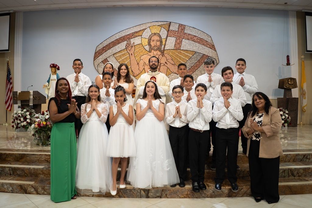 Group of children in white formal attire posing on a stage with a colorful mural backdrop