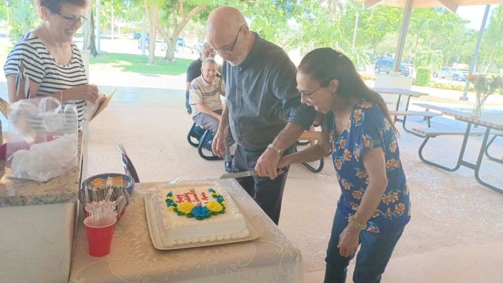 People gathered around a table with a birthday cake under a park pavilion.