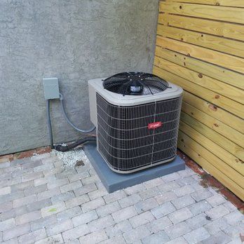 AC unit on a concrete pad next to a wooden fence and gray wall.