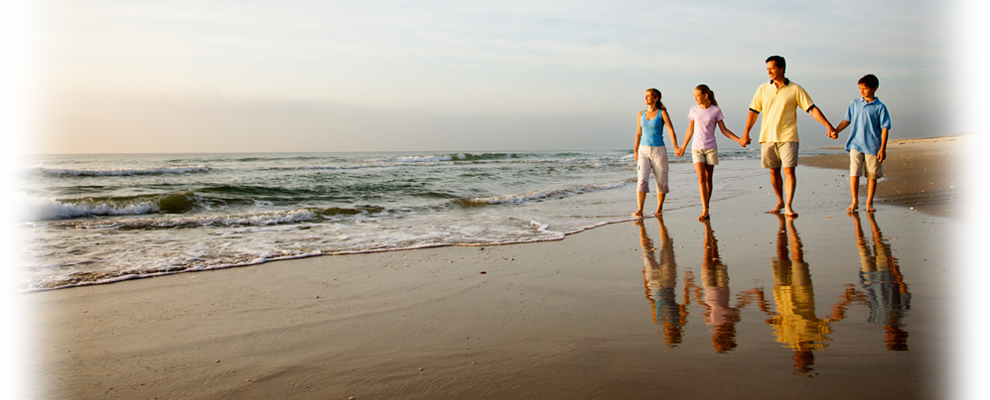 A family is walking on the beach holding hands.