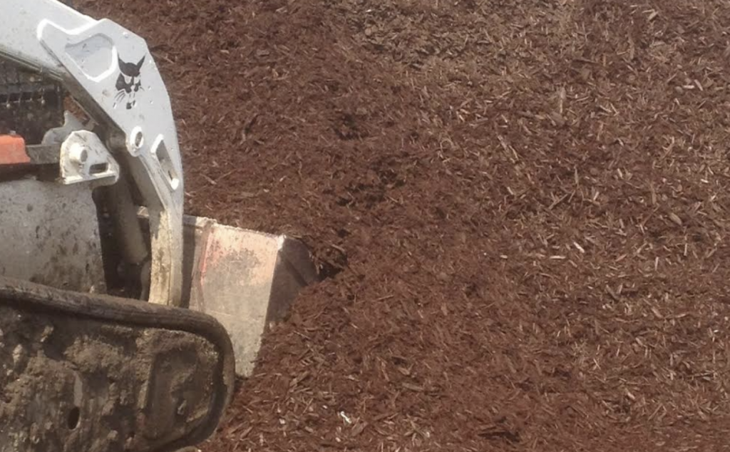 A bobcat tractor is working on a pile of mulch.