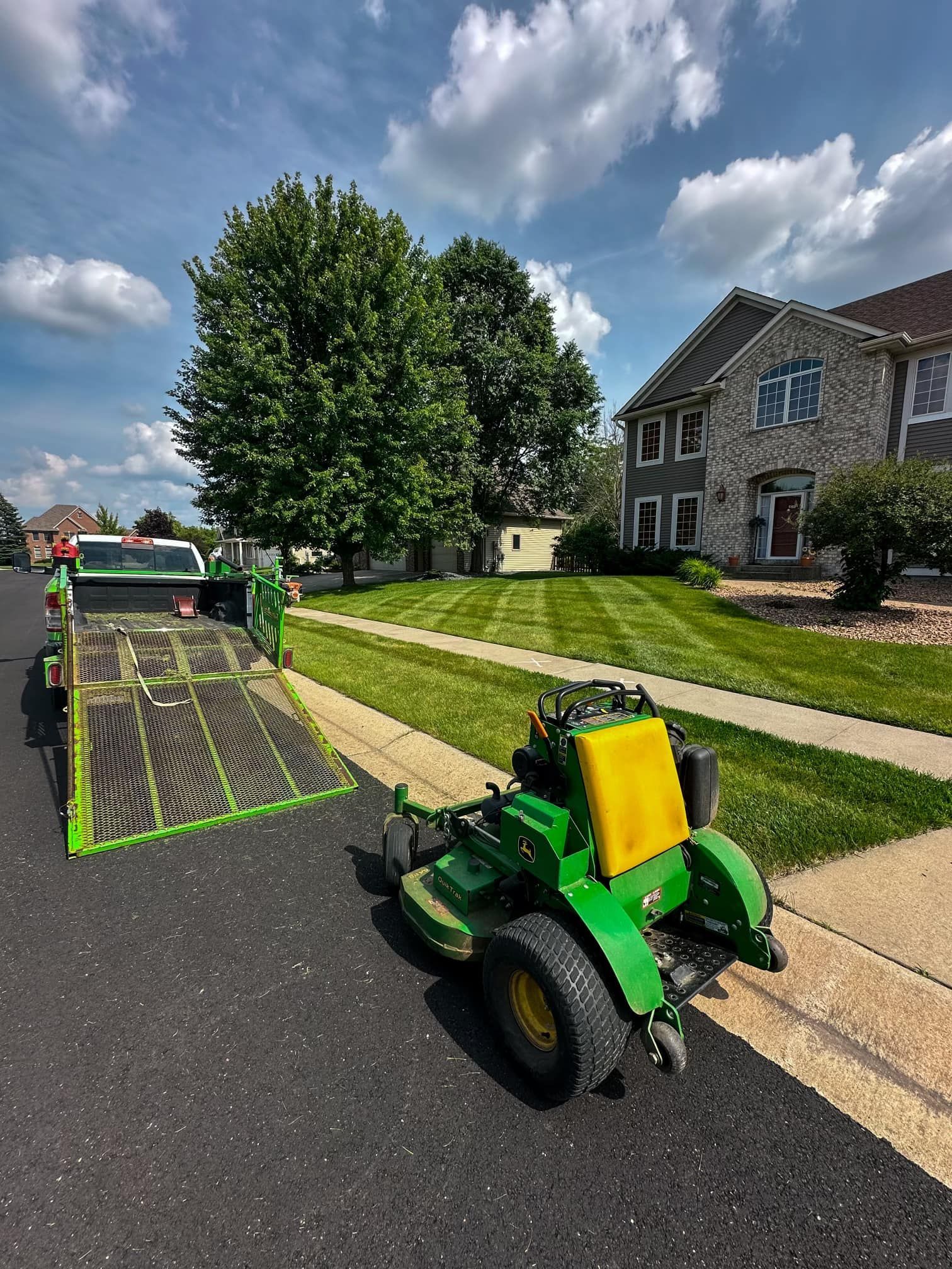 A green lawn mower is parked on the side of the road next to a trailer.