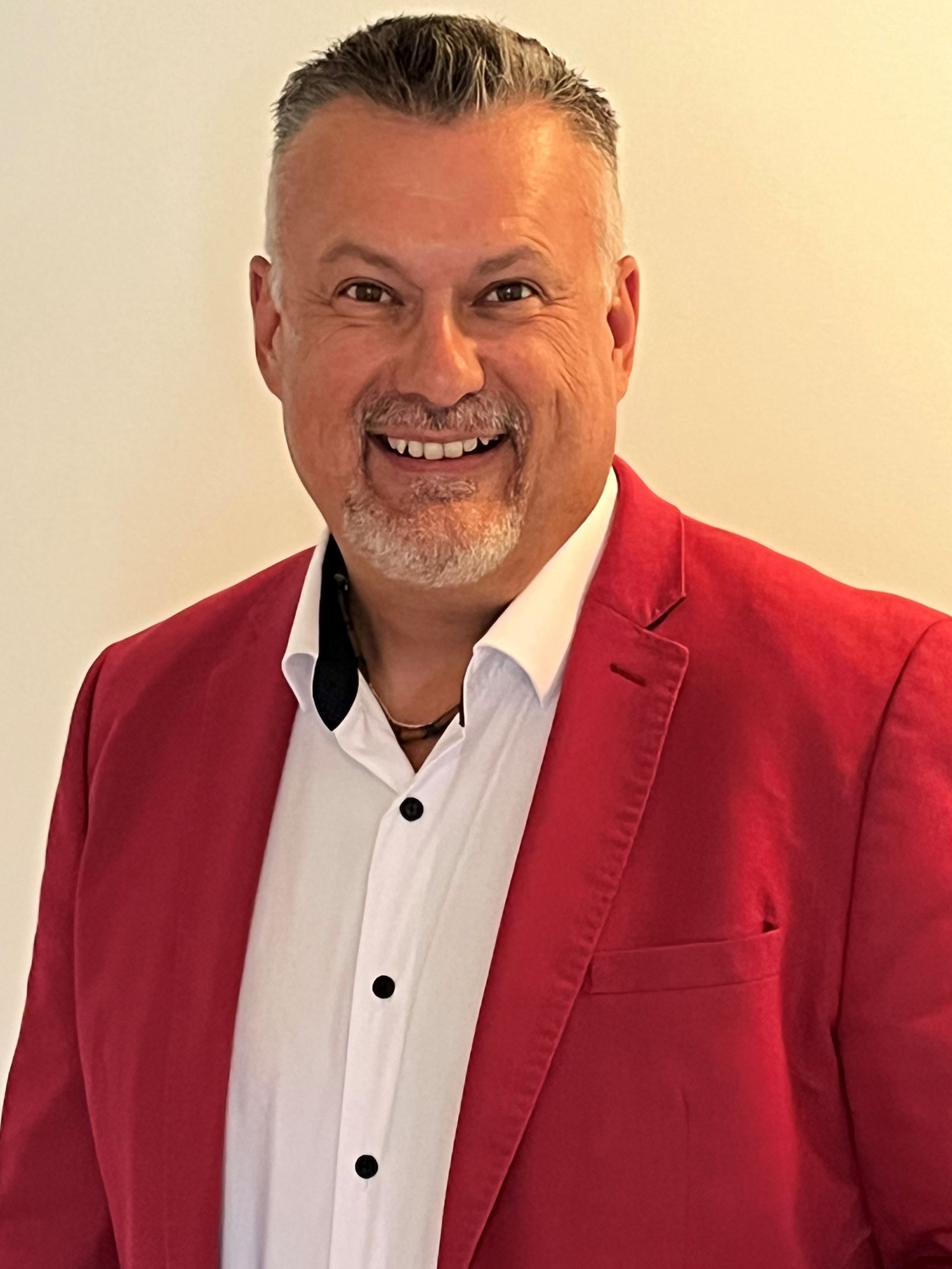 A man in a red jacket and white shirt is smiling for the camera.