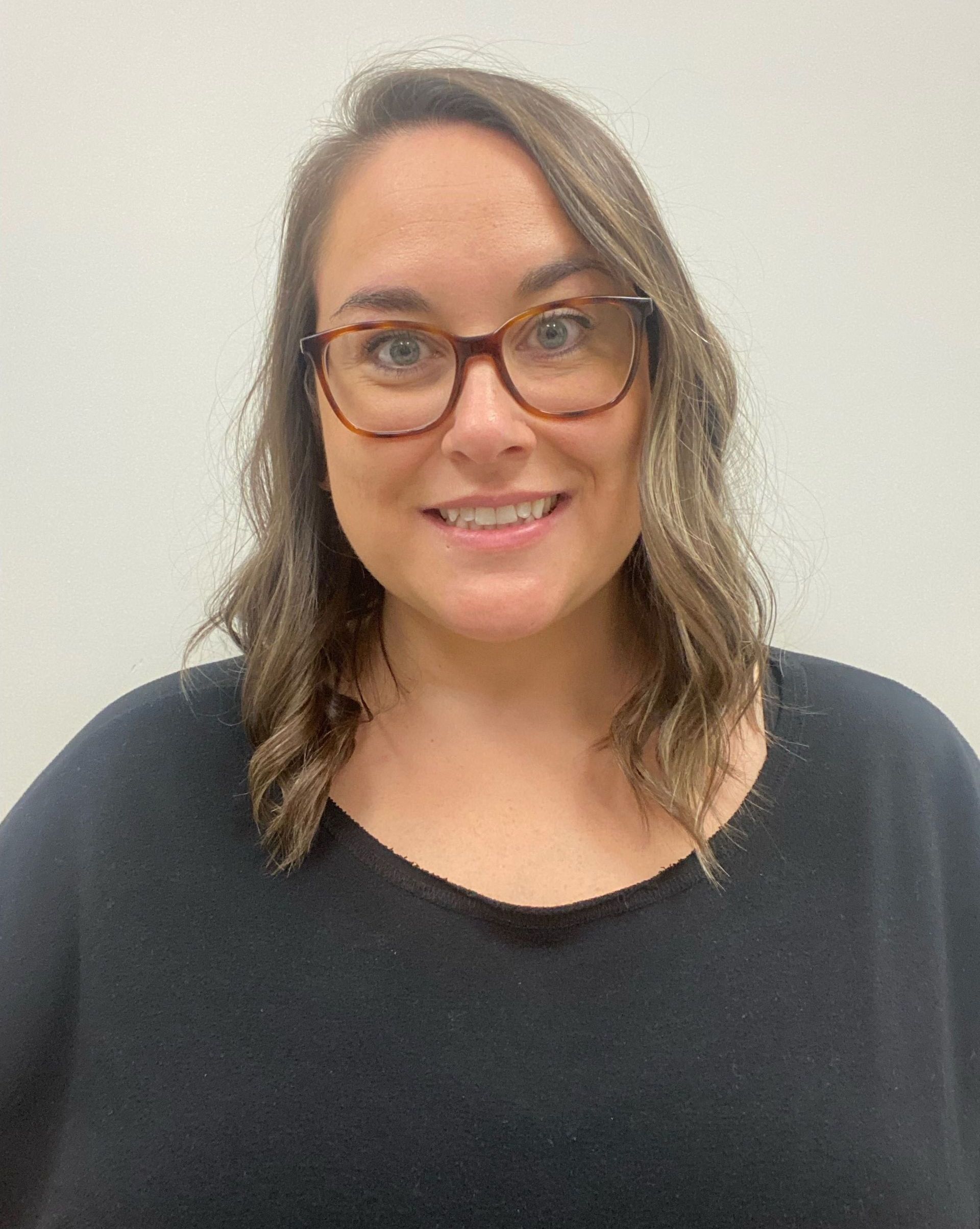 A woman wearing glasses and a black shirt is smiling for the camera.