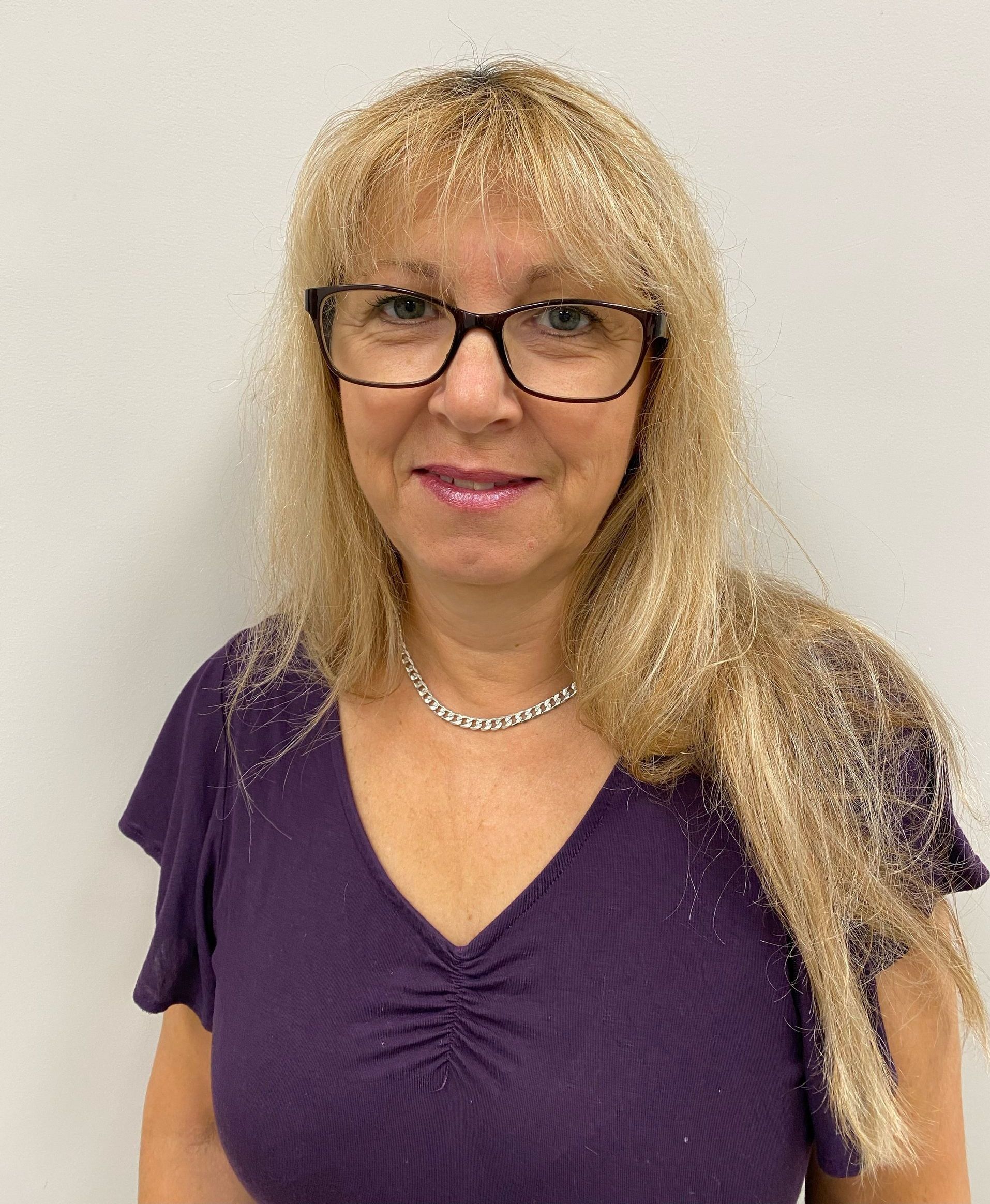 A woman wearing glasses and a purple shirt is smiling for the camera.