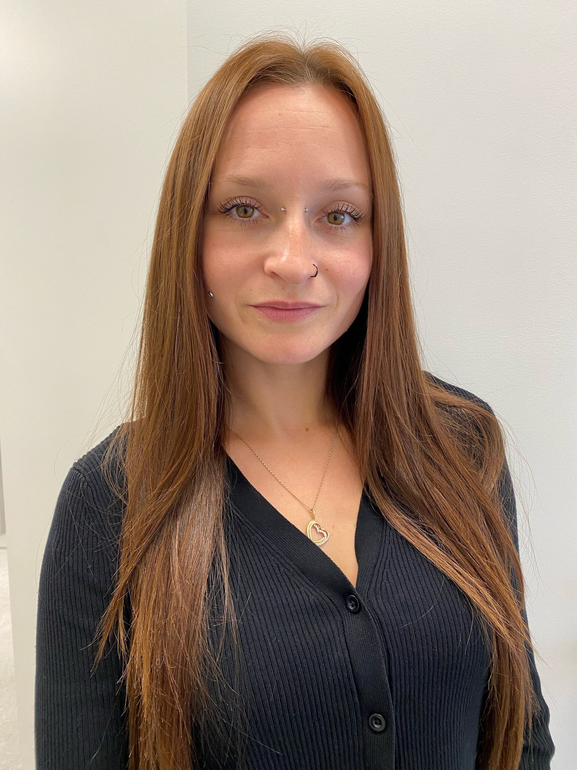A woman with long brown hair is wearing a black sweater and a necklace.