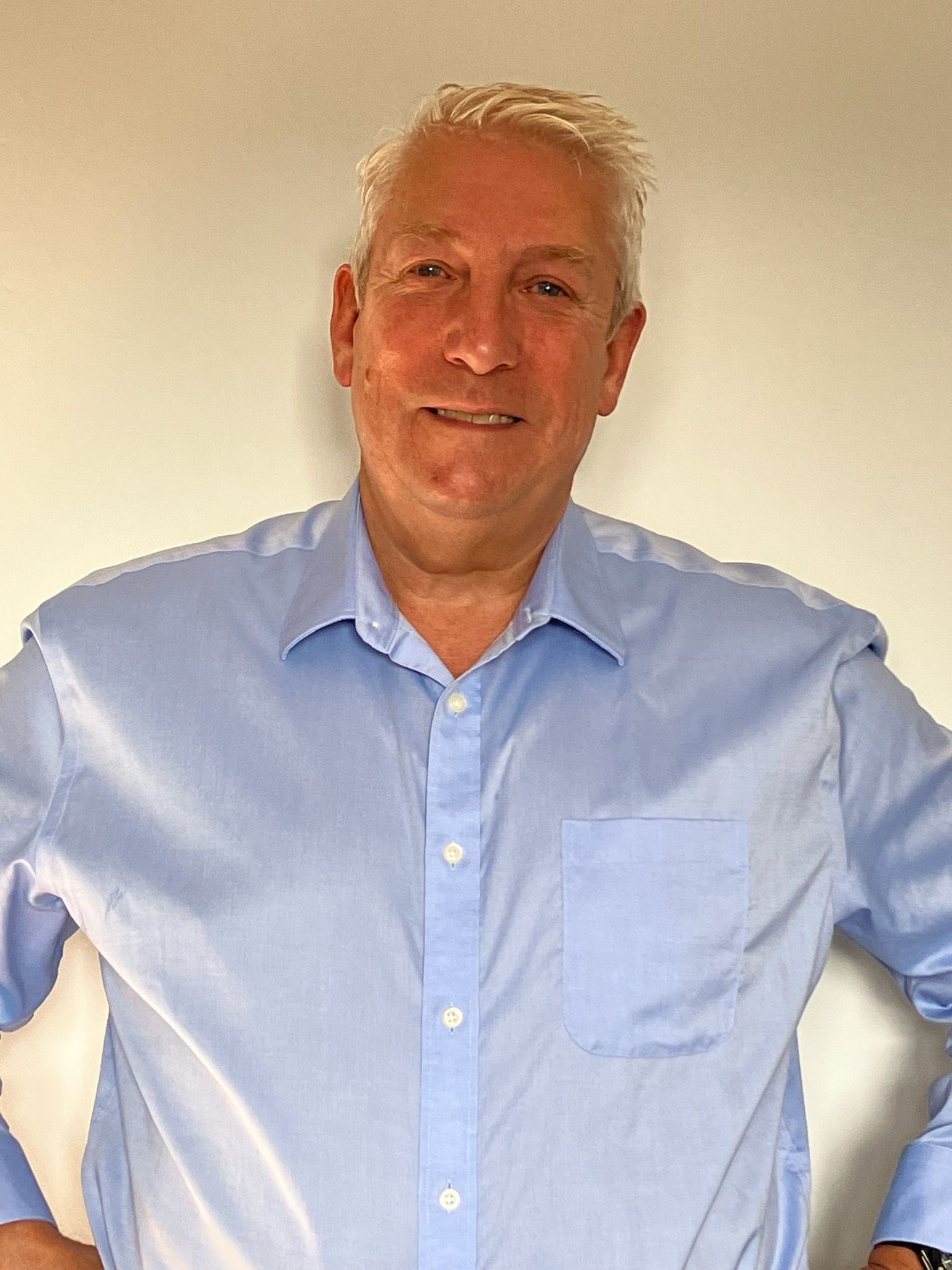 A man in a blue shirt is standing with his hands on his hips.