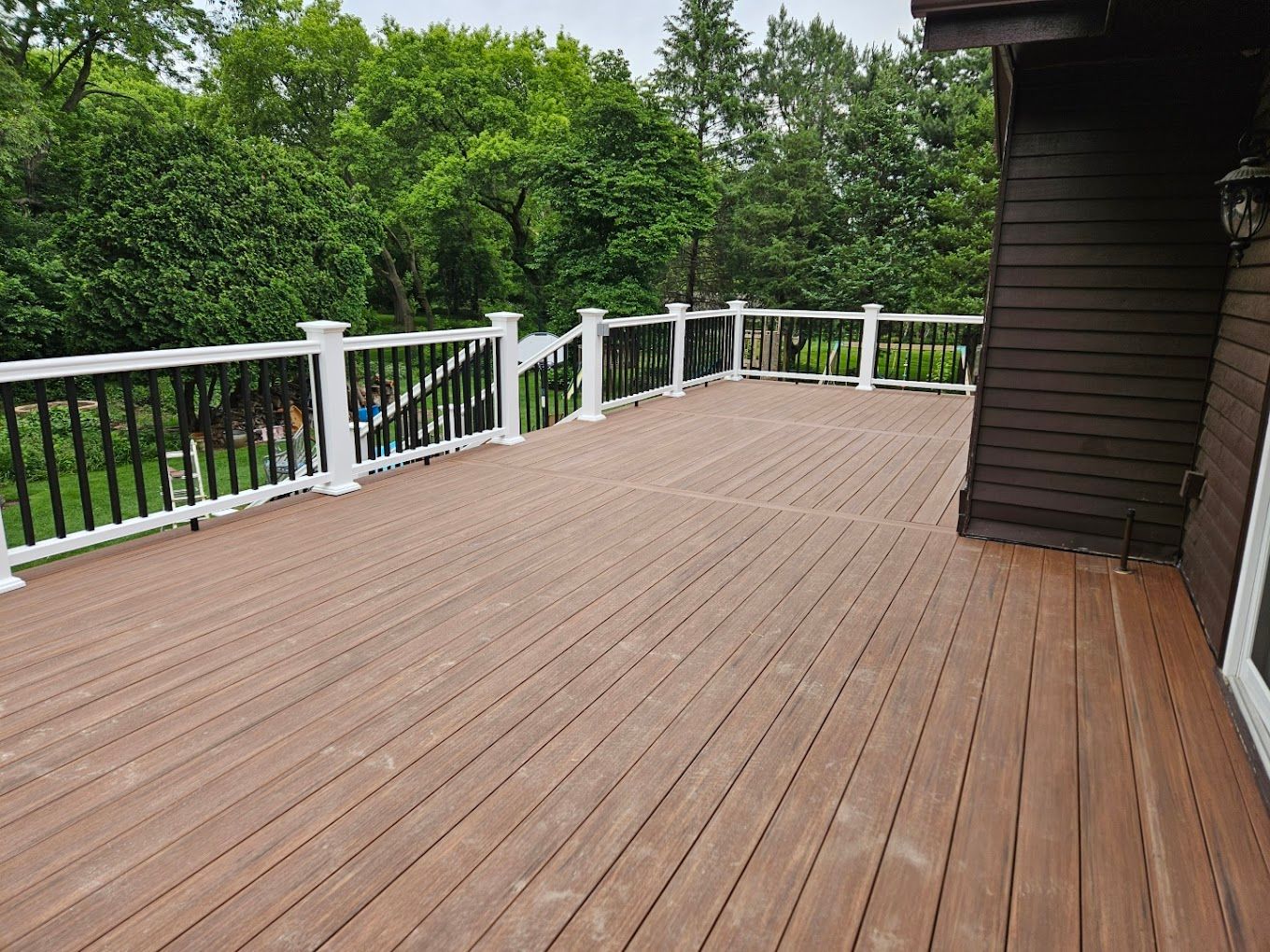 A large wooden deck with a white railing and trees in the background.