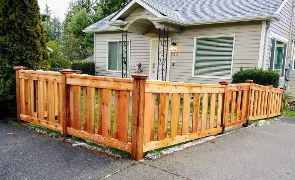 Wooden privacy fence around a small beige house with a covered porch and driveway