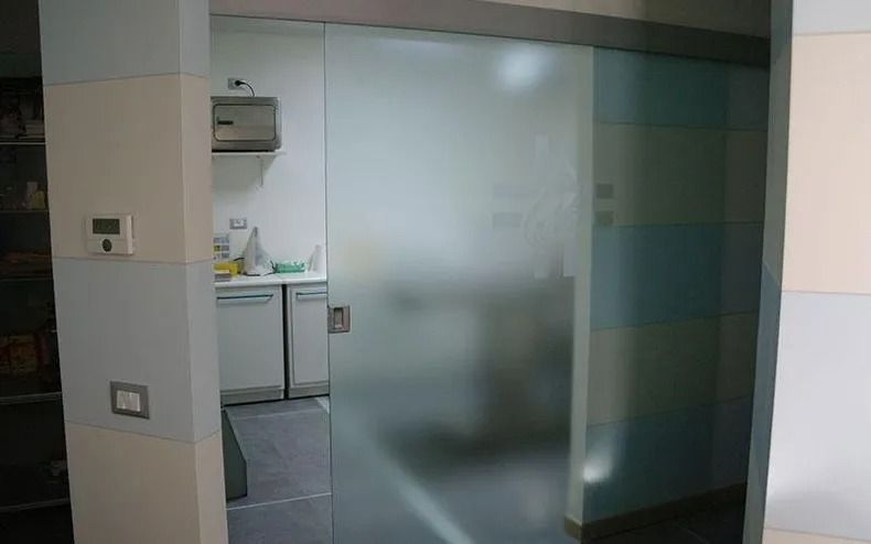 Porta scorrevole in vetro satinato che si apre su una piccola zona cucina con lavello e pensili.
