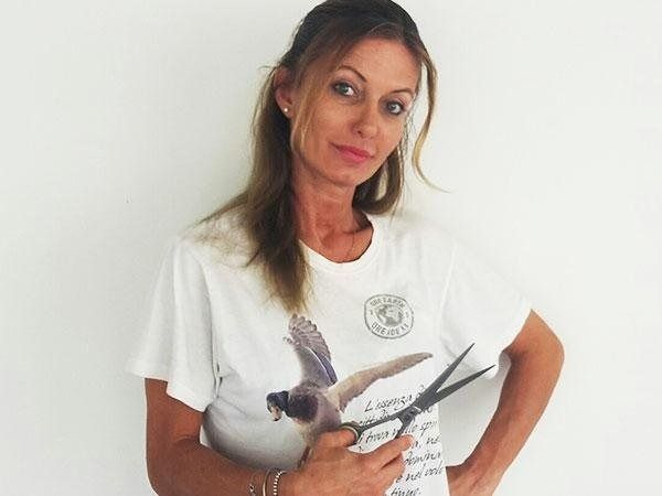Una donna che indossa una maglietta bianca con una stampa grafica è in piedi davanti a una parete bianca.