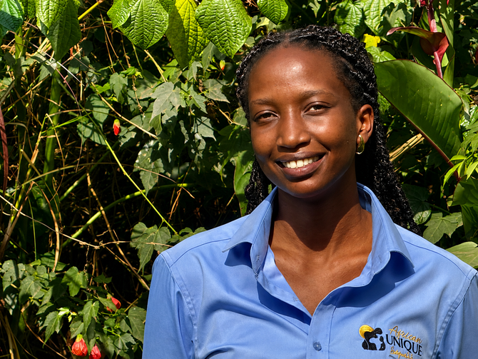 Person smiling in a blue shirt standing in front of green foliage