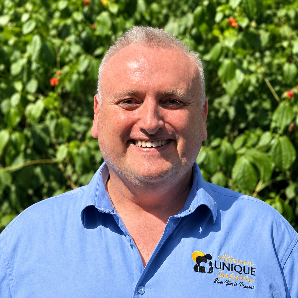 Smiling man in a blue shirt standing in front of green foliage