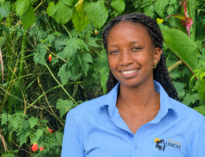 Person smiling in a blue shirt standing in front of green foliage