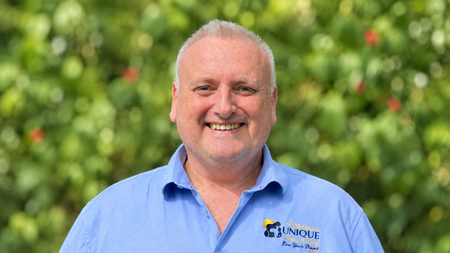 Smiling man in a blue shirt standing in front of green foliage