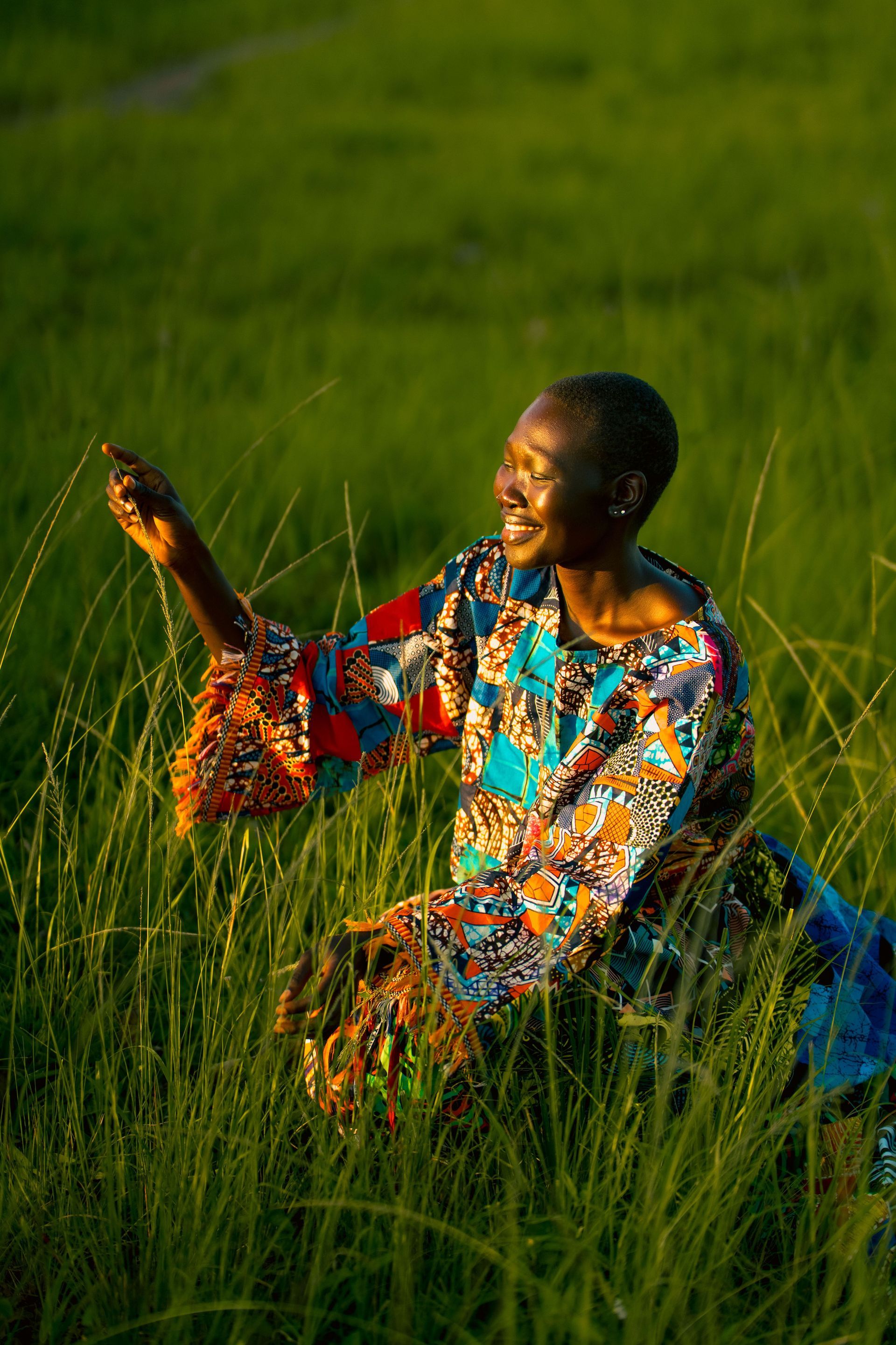 Person in a colorful shirt standing in tall green grass, reaching out and smiling in warm sunlight