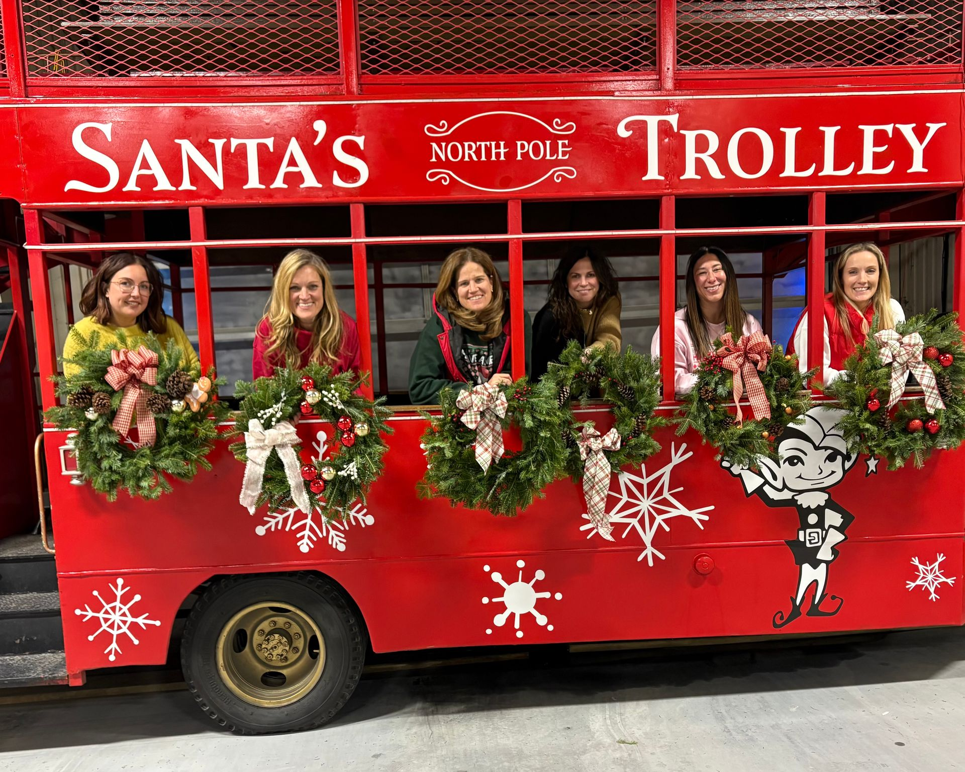People posing in a red Santa trolley decorated with wreaths and holiday ornaments.