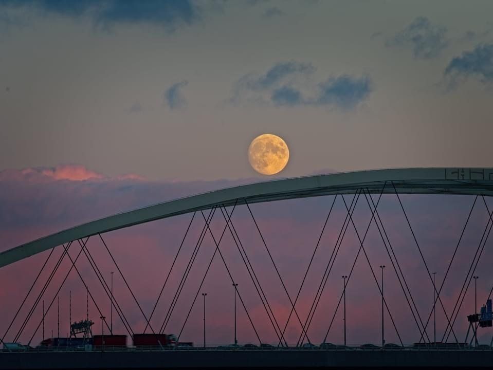 Volle maan komt op boven een brug in de schemering, met een roze en paarse lucht.
