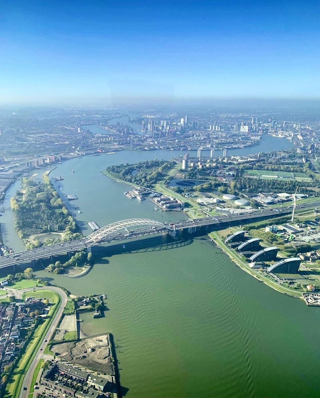 Luchtfoto van Rotterdam, Nederland, met een brug over een brede rivier en een stadsgezicht op de achtergrond.