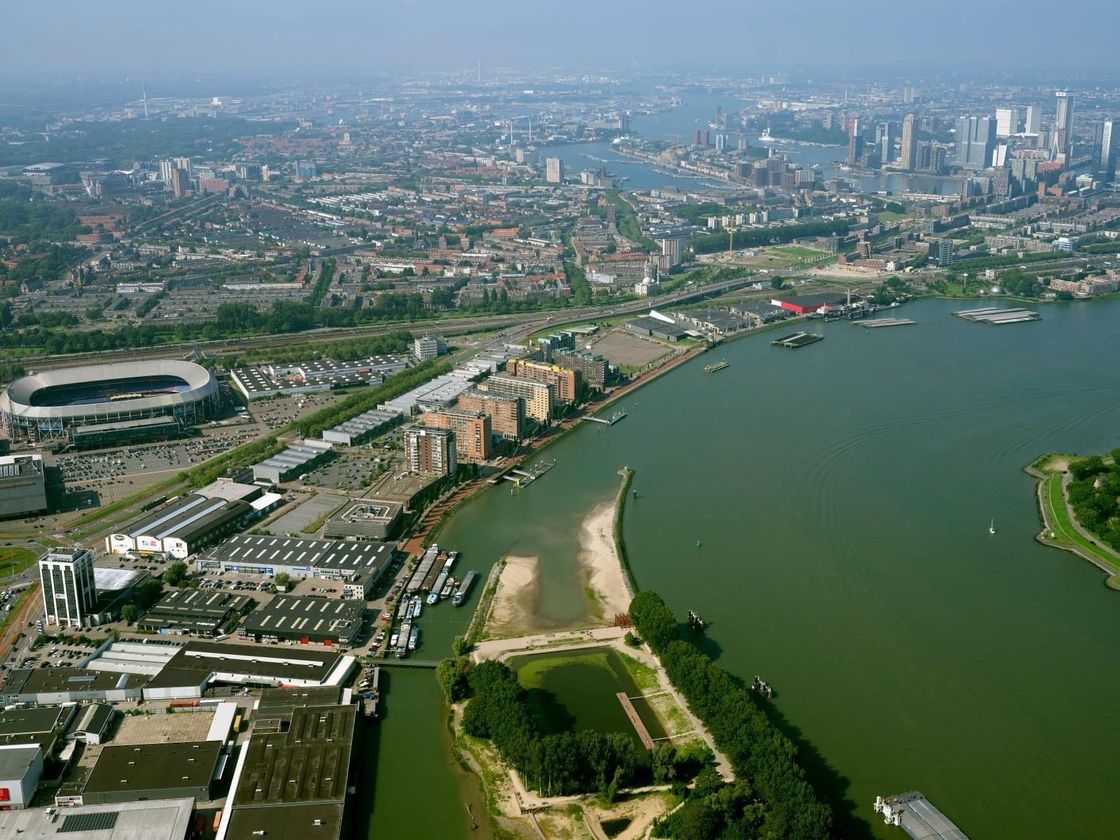 Luchtfoto van een stad met een rivier; gebouwen, een stadion en boten zijn zichtbaar.