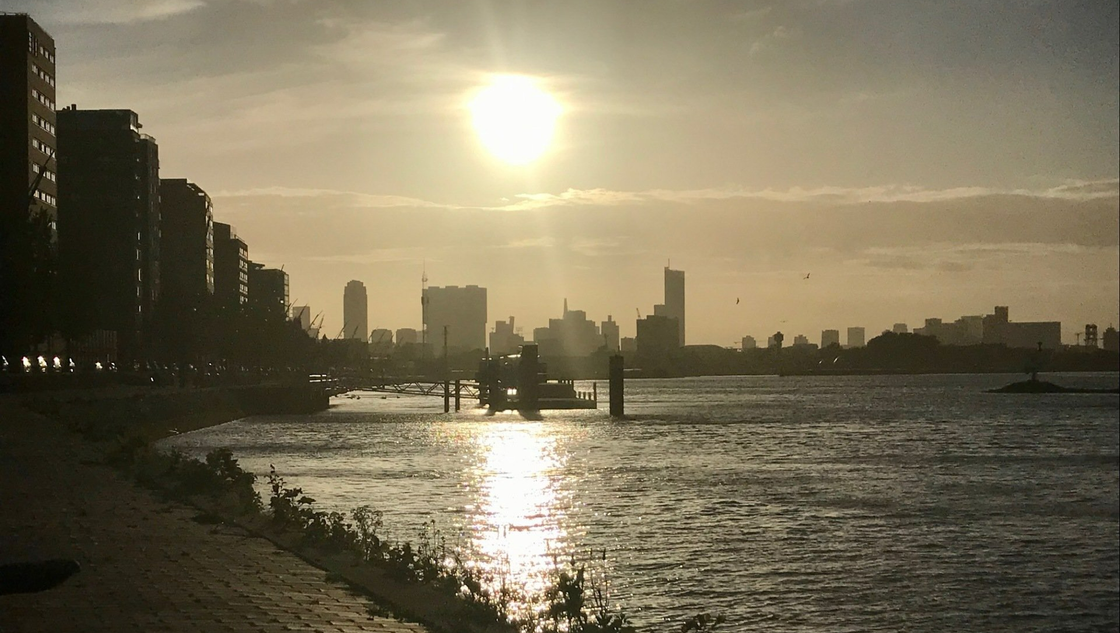 De zon gaat onder boven een stadsgezicht en het water. Gebouwen staan ​​langs de kust, de zon weerkaatst op het water.