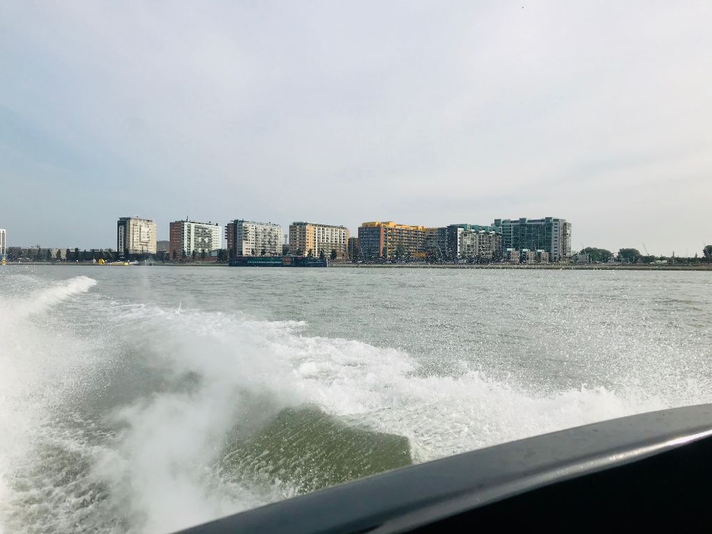 Een boot vaart over het water richting de skyline van een stad onder een bewolkte hemel.