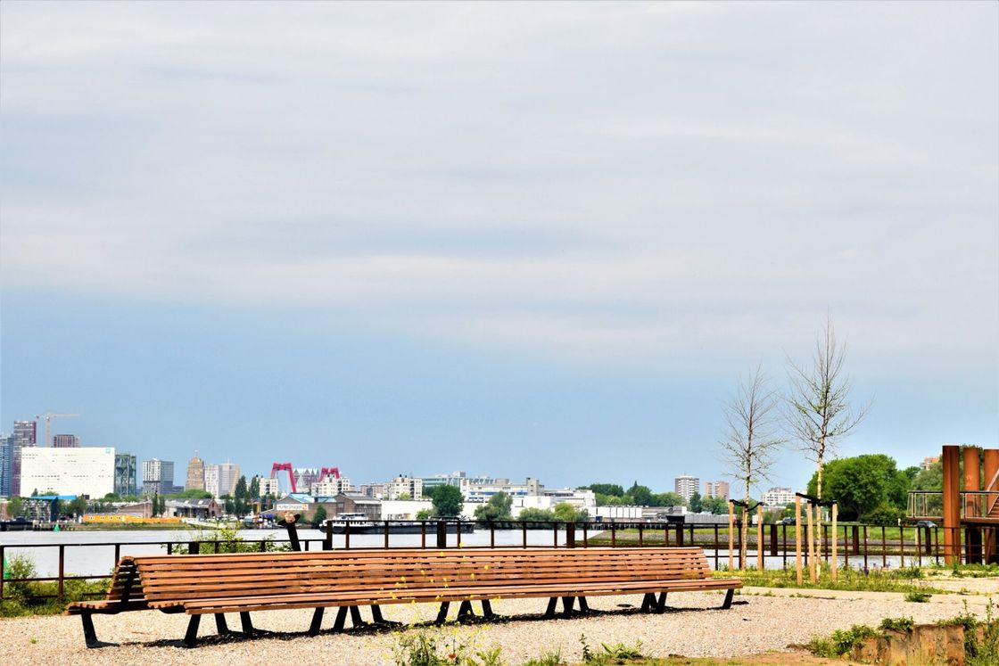 Houten bank met uitzicht op een rivier en de skyline van de stad onder een bewolkte hemel.