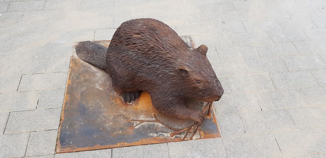 Een roestig metalen beverbeeld op een verweerde vierkante sokkel op een bakstenen ondergrond.