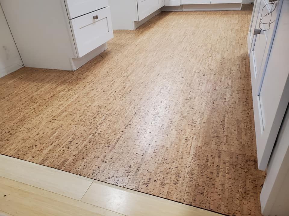 A kitchen with a cork floor and white cabinets.