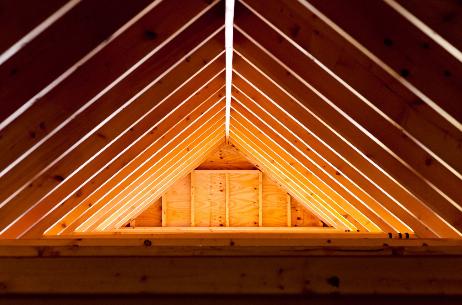 Wooden roof trusses forming a triangle, light shining through.