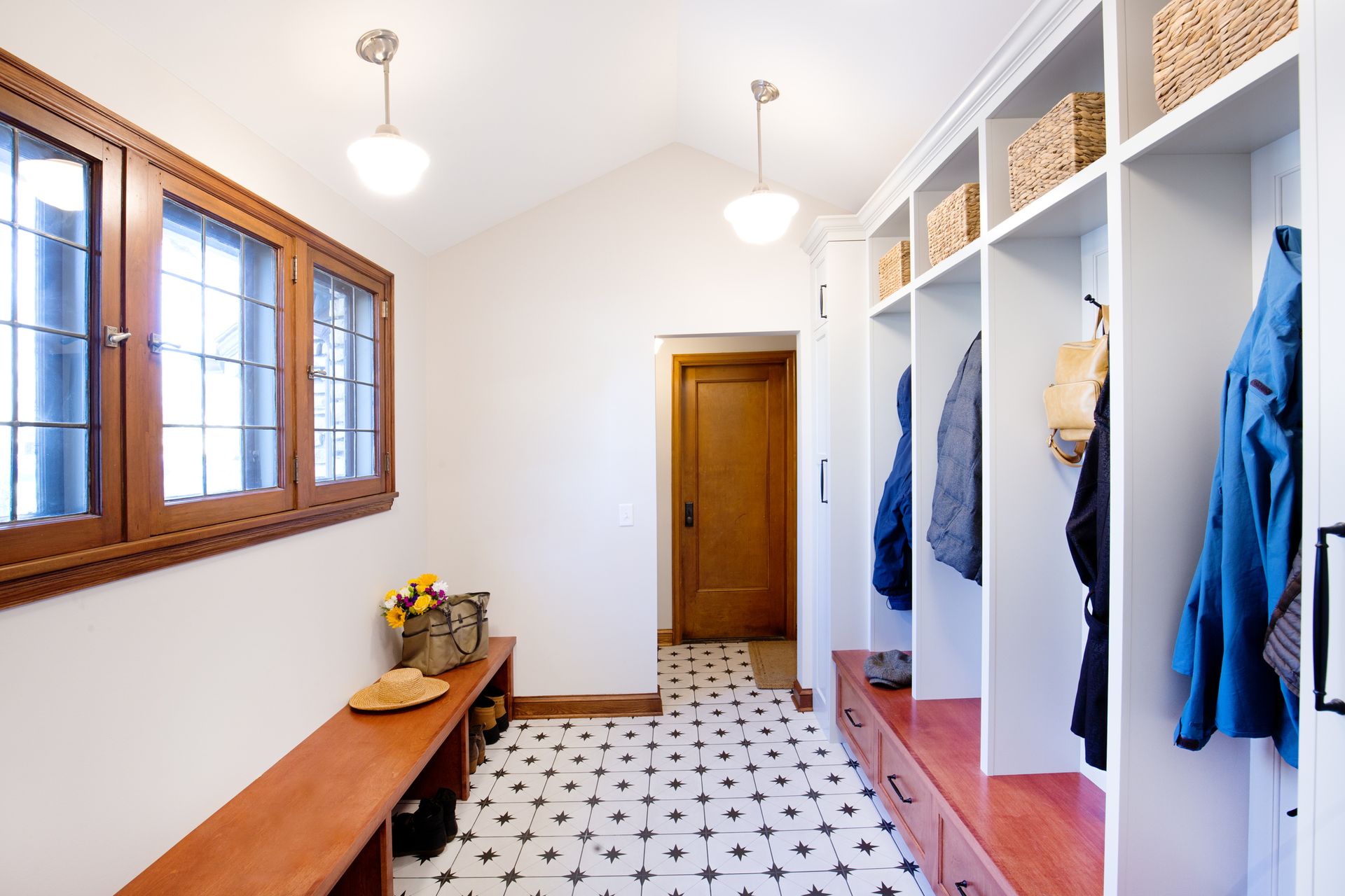 Mudroom with white lockers, wooden bench, and black and white tile floor.
