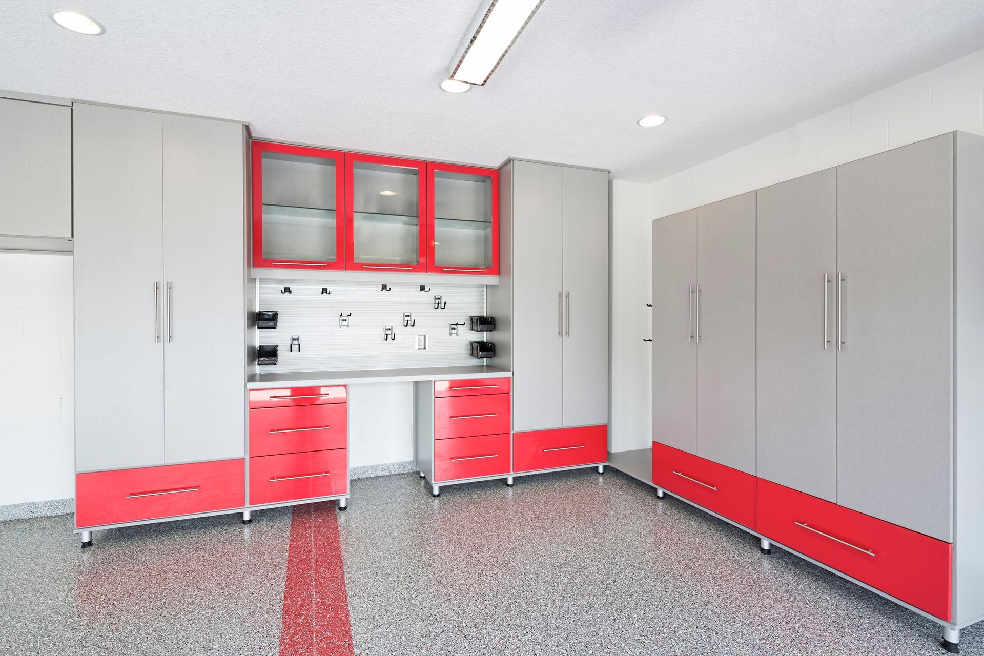 Garage with gray cabinets and red accents. Storage space with desk.