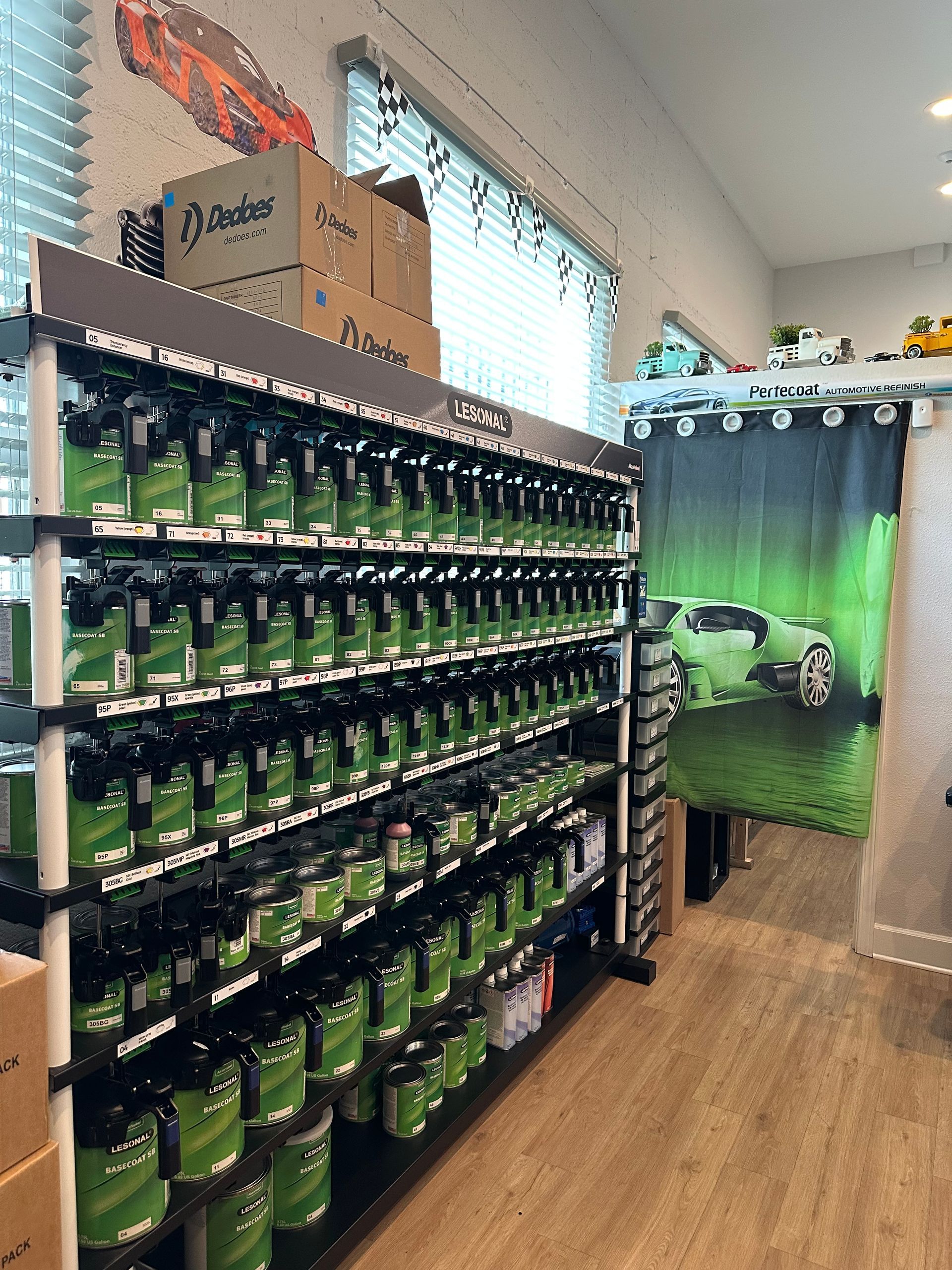 Shelves filled with green paint cans inside a store, with a car graphic on a curtain.