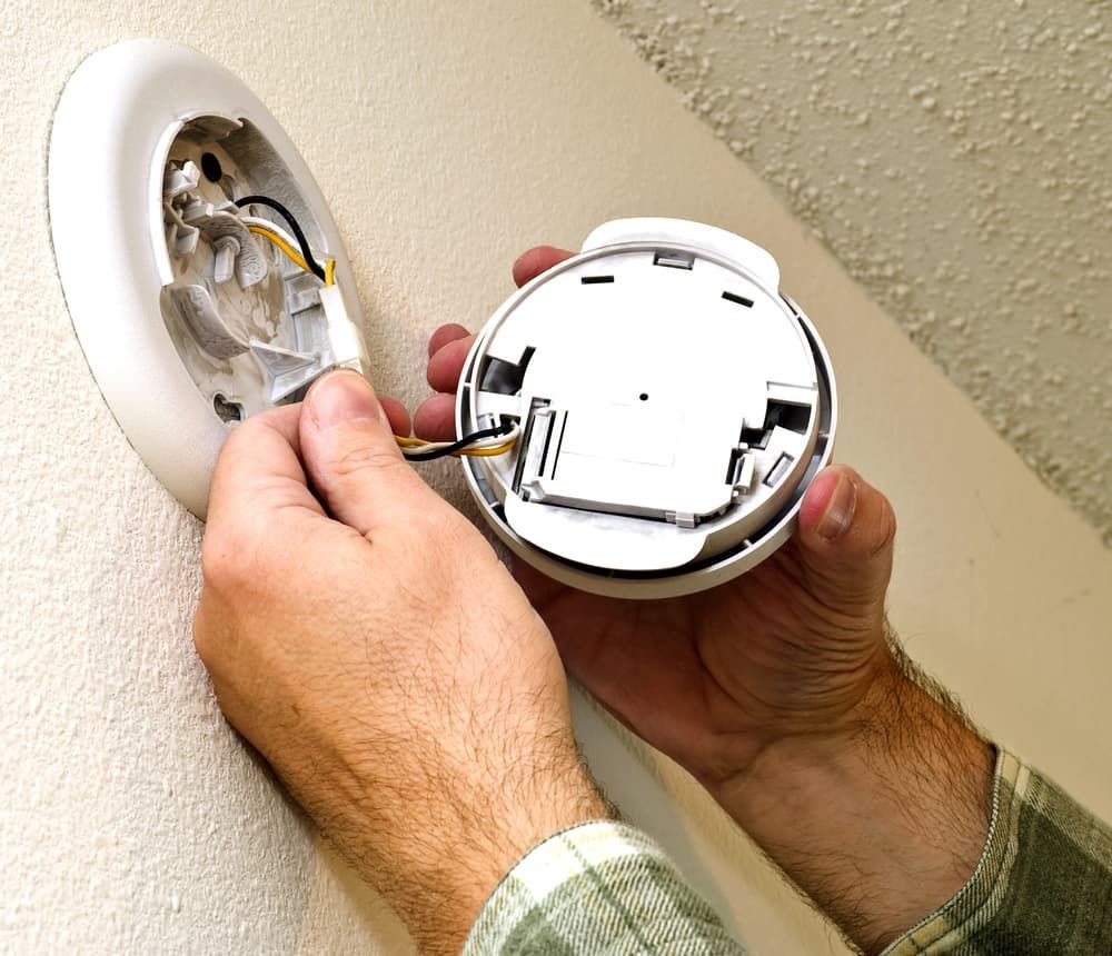 A Man Is Installing a Smoke Detector on A Wall — Jason Wenta Electrical Services in Condon, QLD