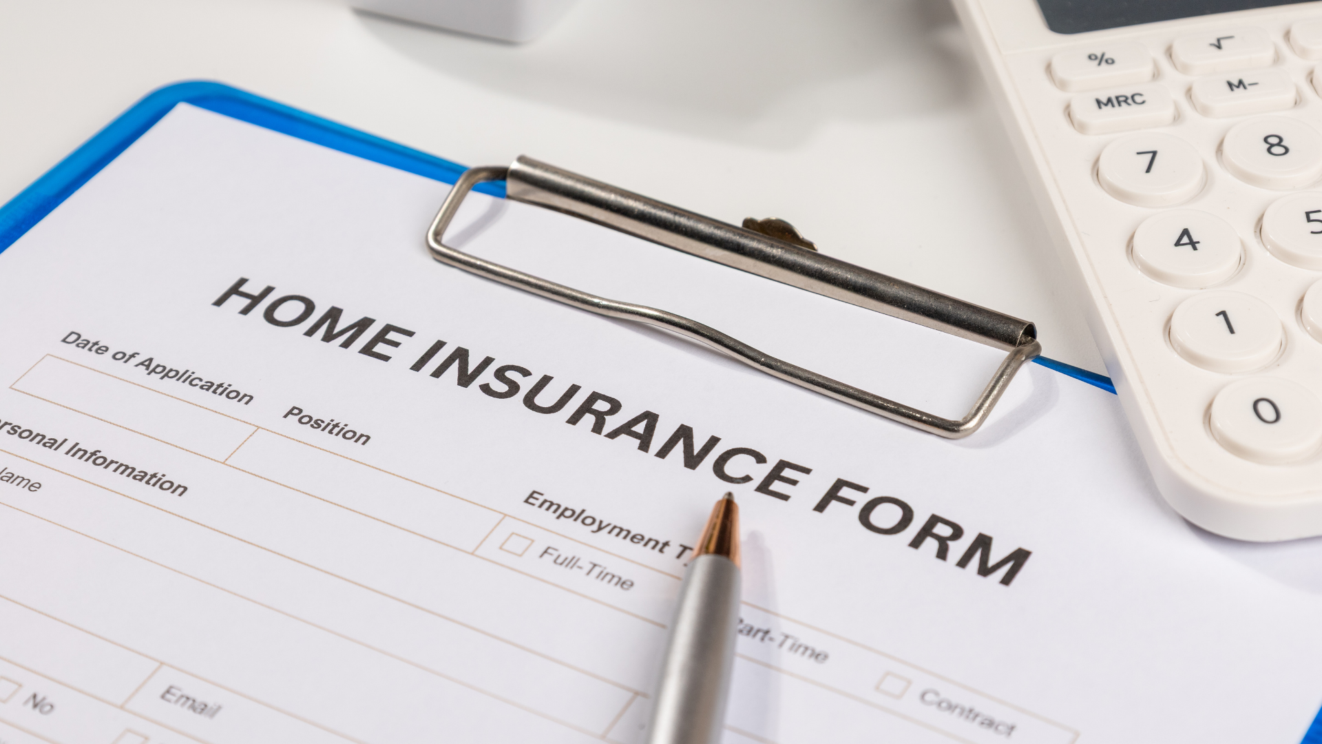 A home insurance form on a clipboard with a pen and a calculator on a desk.