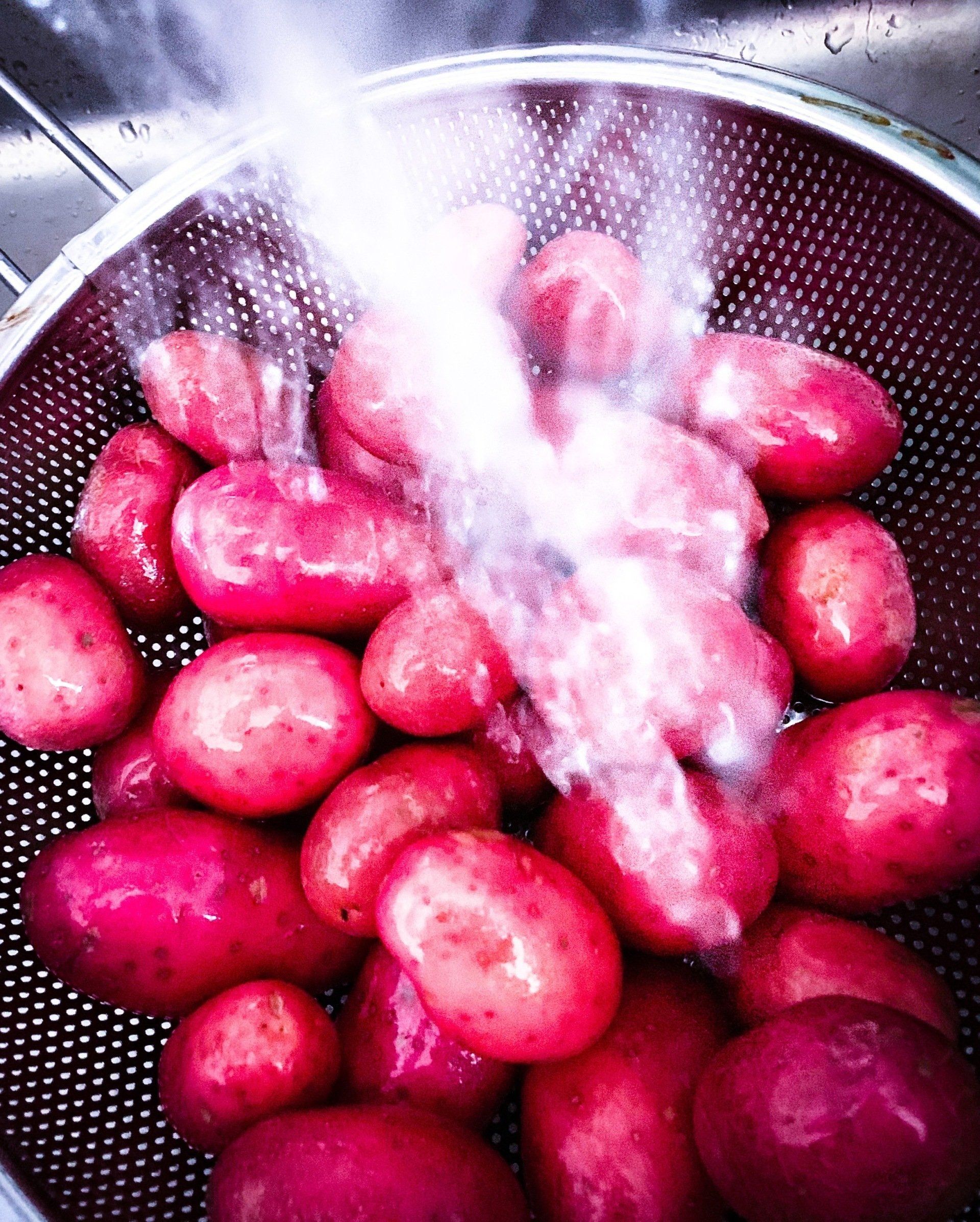 Rode aardappelen worden in een metalen vergiet onder stromend water afgespoeld.