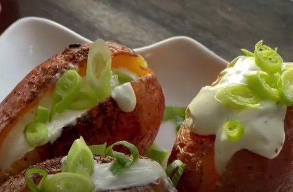 Gevulde geroosterde paprika's, overgoten met gesmolten witte saus en gesneden groene uitjes, geserveerd op een wit bord.